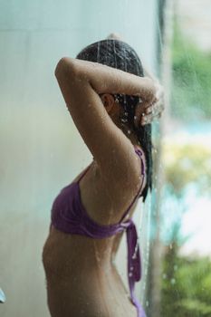 Side view of unrecognizable slim brunette in swimsuit washing hair in water stream outdoors near swimming pool