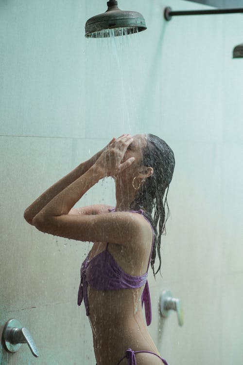 Sensual woman in bikini under stream in shower