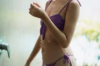 Crop unrecognizable slim woman wearing swimsuit standing and enjoying refreshing water stream in spa center on blurred background