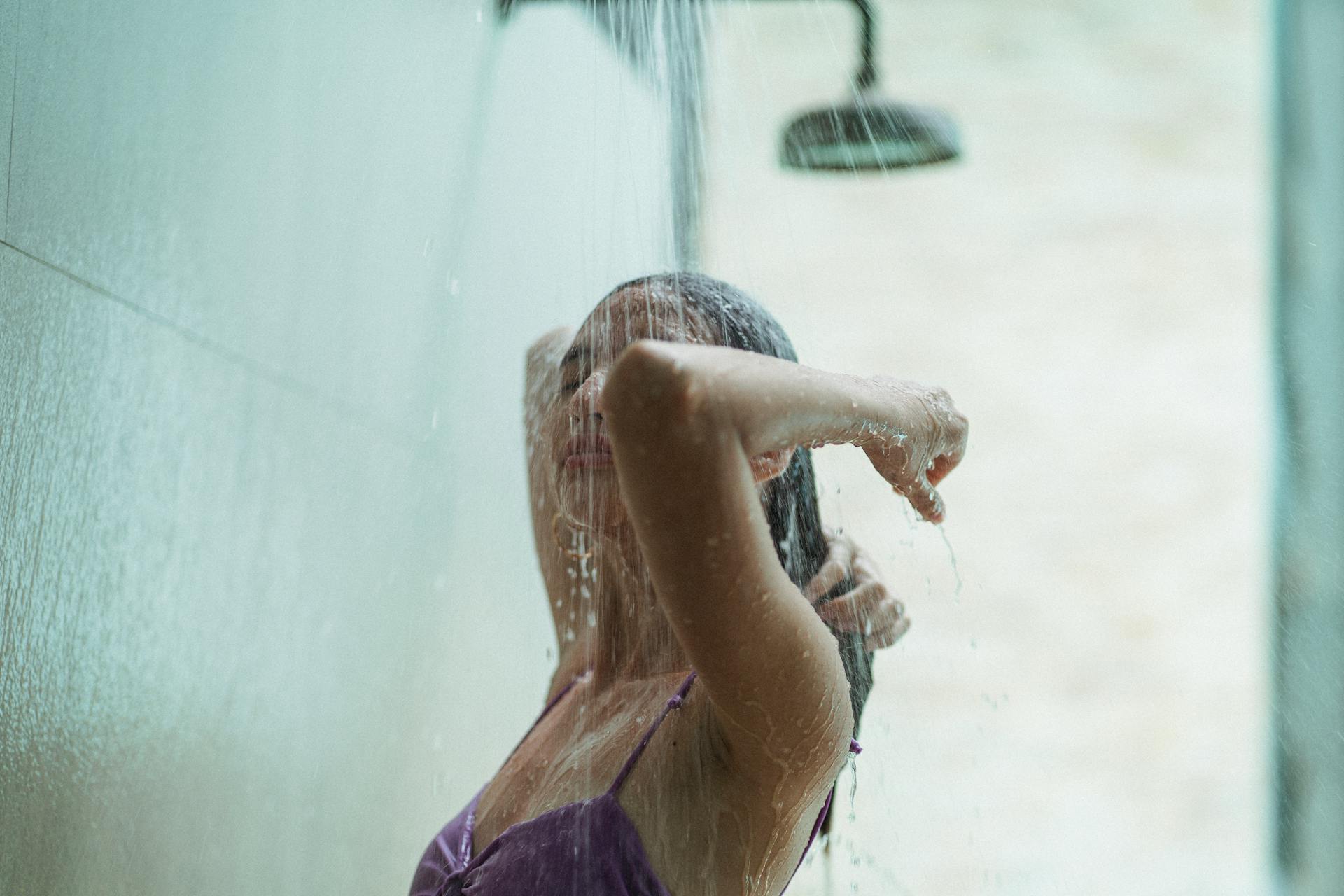 Young female in swimsuit rinsing hair in shower