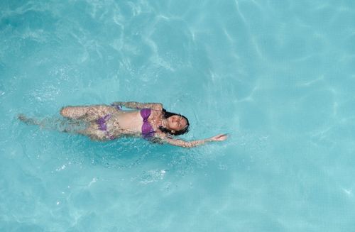 Free From above of young slim woman in violet bikini floating on back in crystal clear seawater on sunny summer day Stock Photo