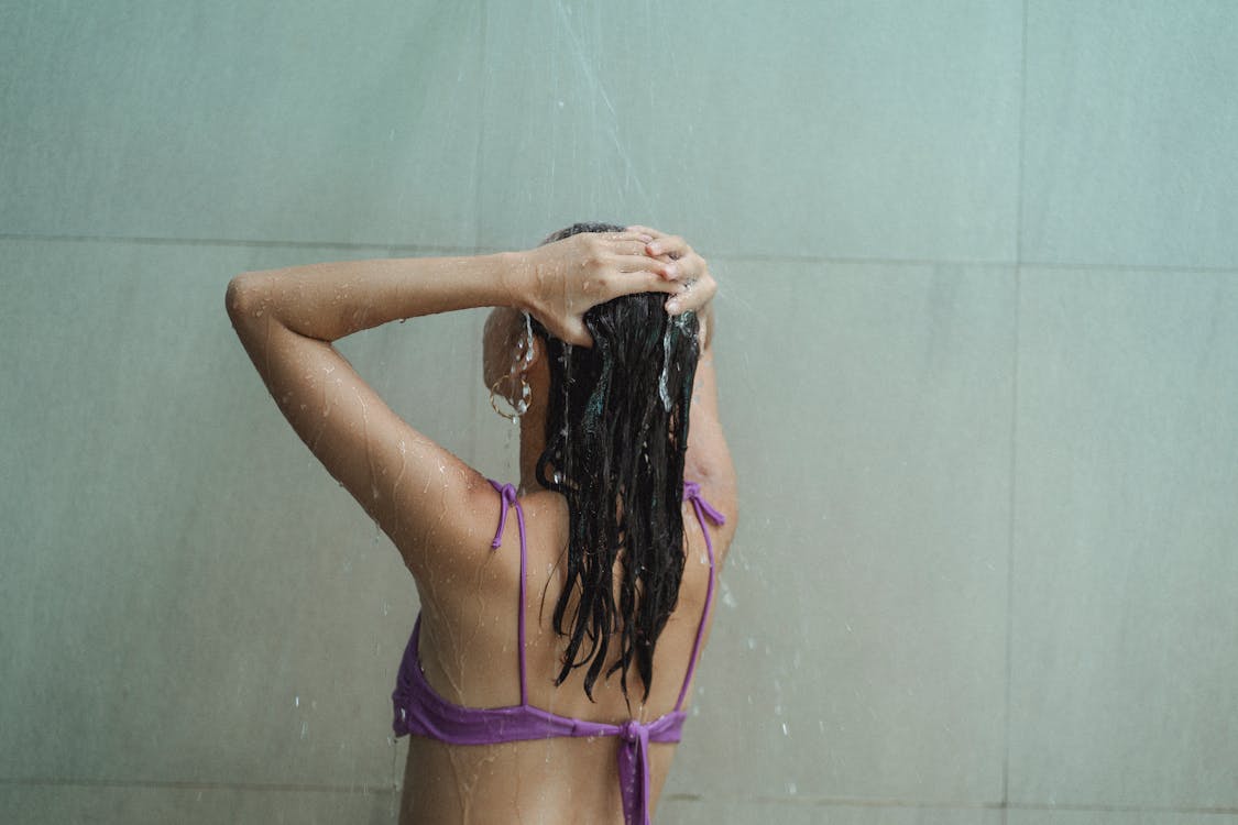 Slim woman in bikini washing head in spacious bathroom