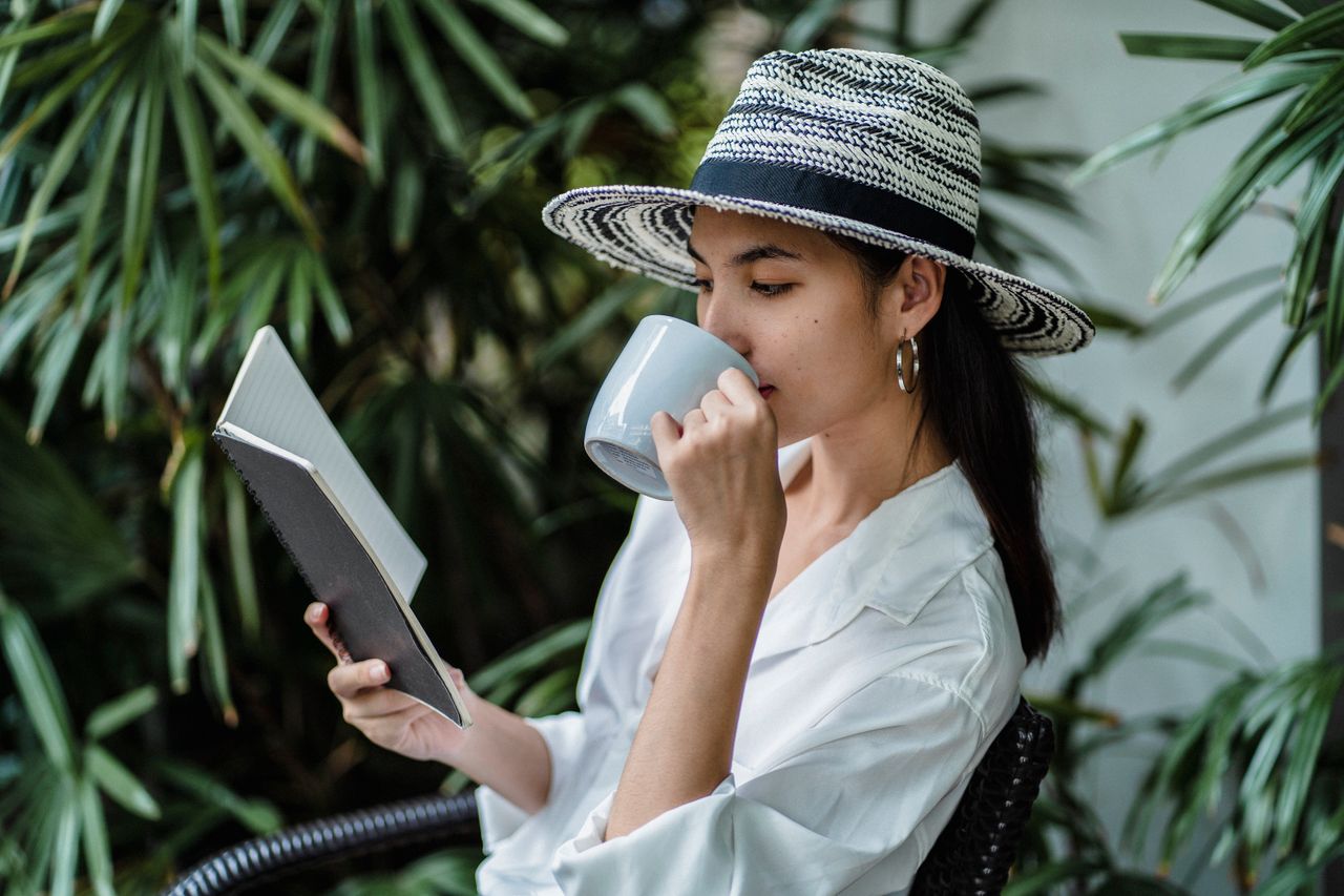 thoughtful asian female in stylish white shirt and straw hat reading n