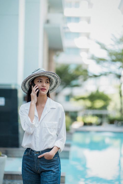 Free Stylish lady in hat standing near modern pool and speaking on smartphone on sunny day Stock Photo