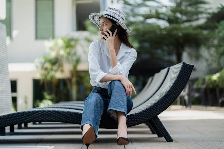 Pensive Young Asian Lady Talking On Smartphone In Hotel Yard