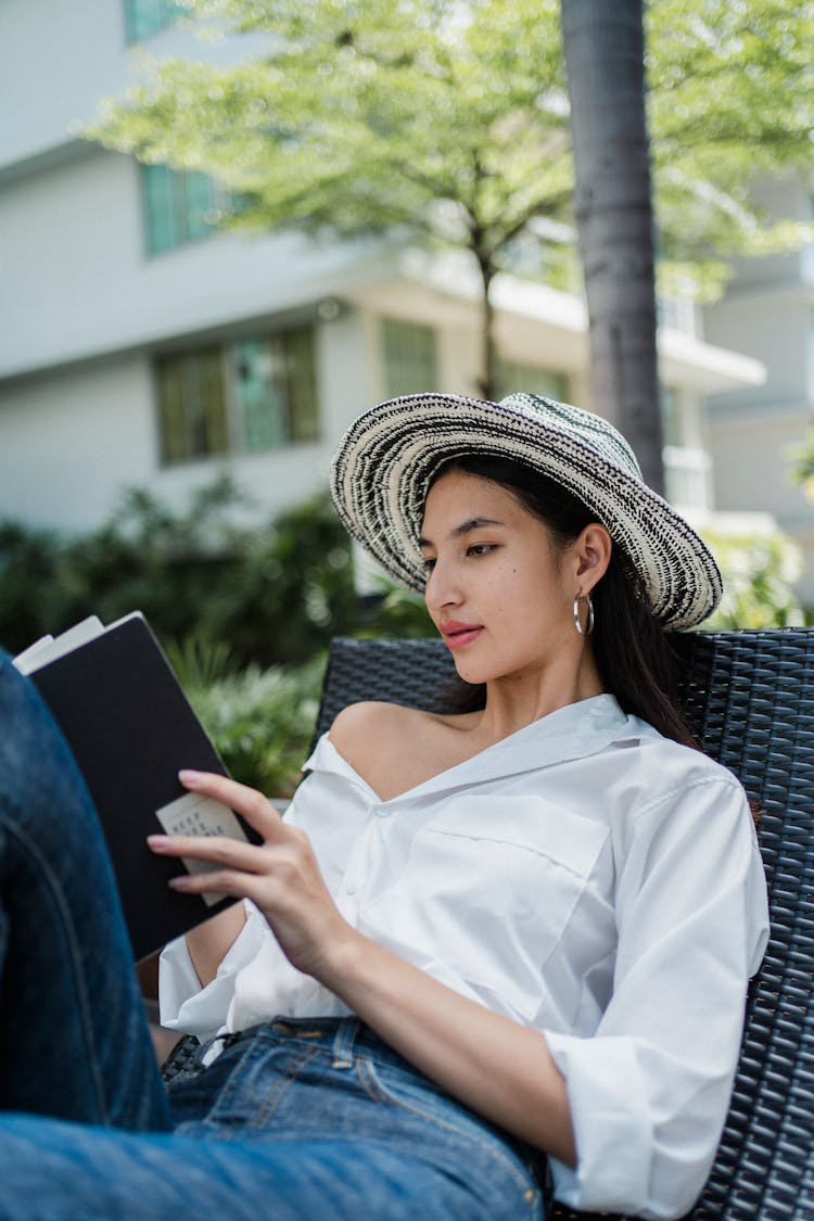 Relaxed Young Asian Woman Reading Book In Hotel Patio