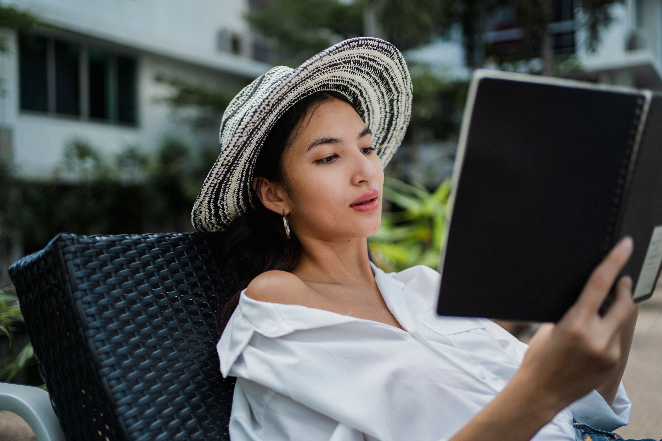 Solo woman in straw hat reviewing notes on a sunbed before checking into a vacation rental Solo woman in straw hat reviewing notes on a sunbed before checking into a vacation rental