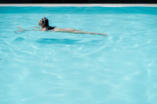 Free Side view full body of female tourist swimming in pool with crystal clear water at resort Stock Photo
