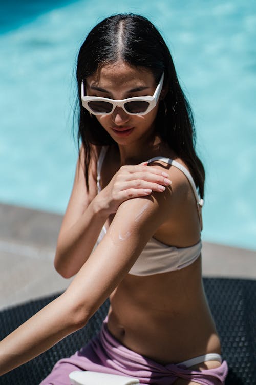 From above of female wearing sunglasses and bikini relaxing on deckchair on poolside at resort