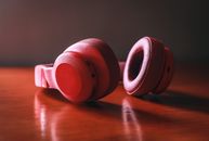 Close-up of red wireless headphones resting on a wooden surface, highlighting sleek design and vibrant color.