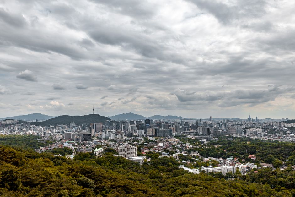 A high-angle shot of Seoul's skyline under a cloudy sky, showcasing the urban landscape.
