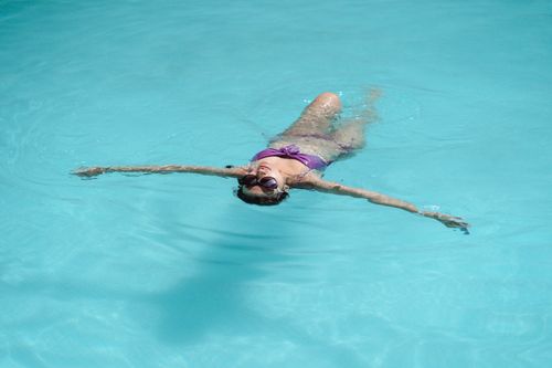 Free From above of unrecognizable young slim female tourist in bikini and sunglasses floating in swimming pool on sunny summer day Stock Photo