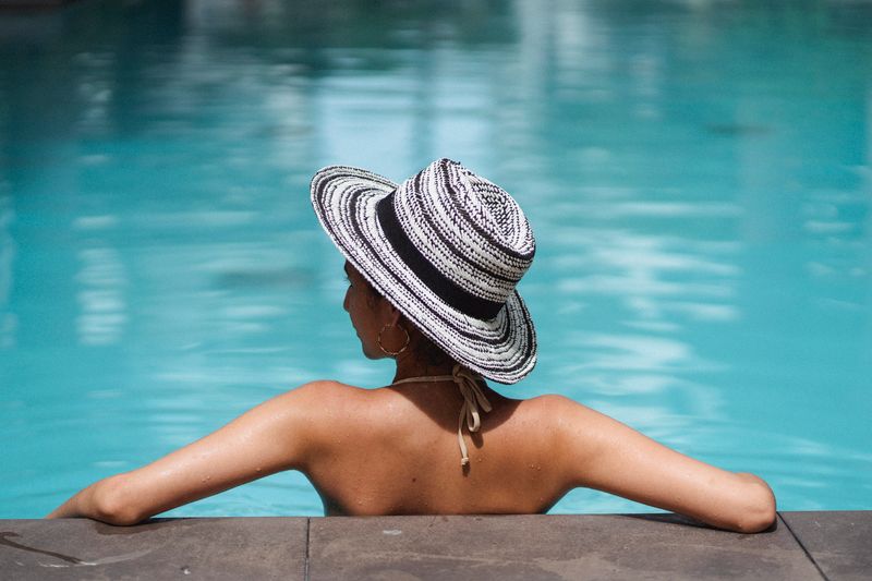 A woman wearing a straw hat enjoying a serene moment by the poolside, basking in the summer sun.