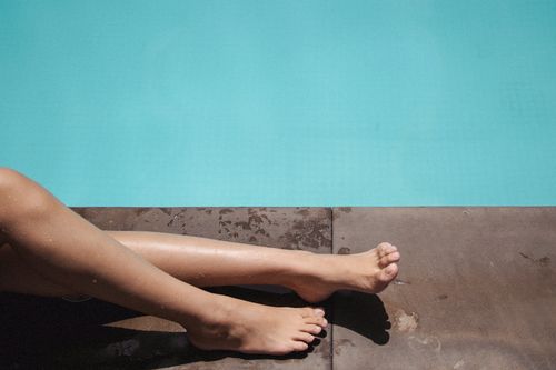 Free From above of crop anonymous barefoot female sunbathing lying on border of swimming pool Stock Photo