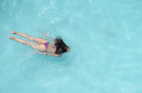 Free From above back view of unrecognizable sensual female traveler with long dark hair in stylish bikini swimming in pool on sunny day Stock Photo