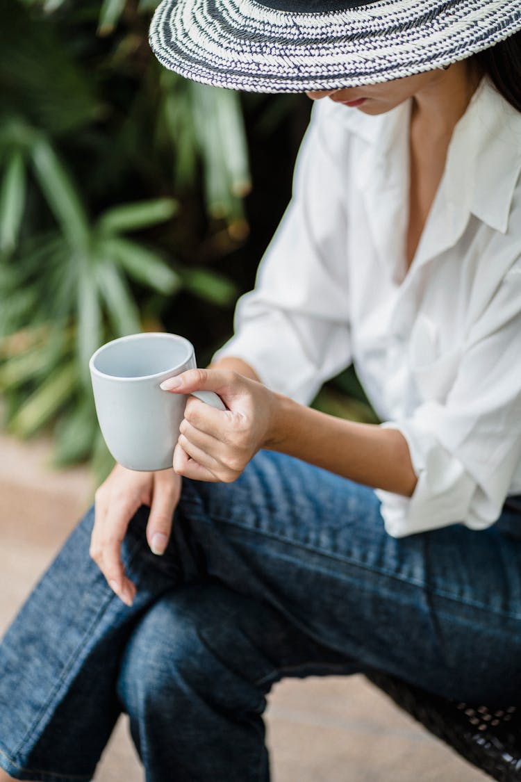 Unrecognizable Young Woman Relaxing In Garden With Cup Of Coffee