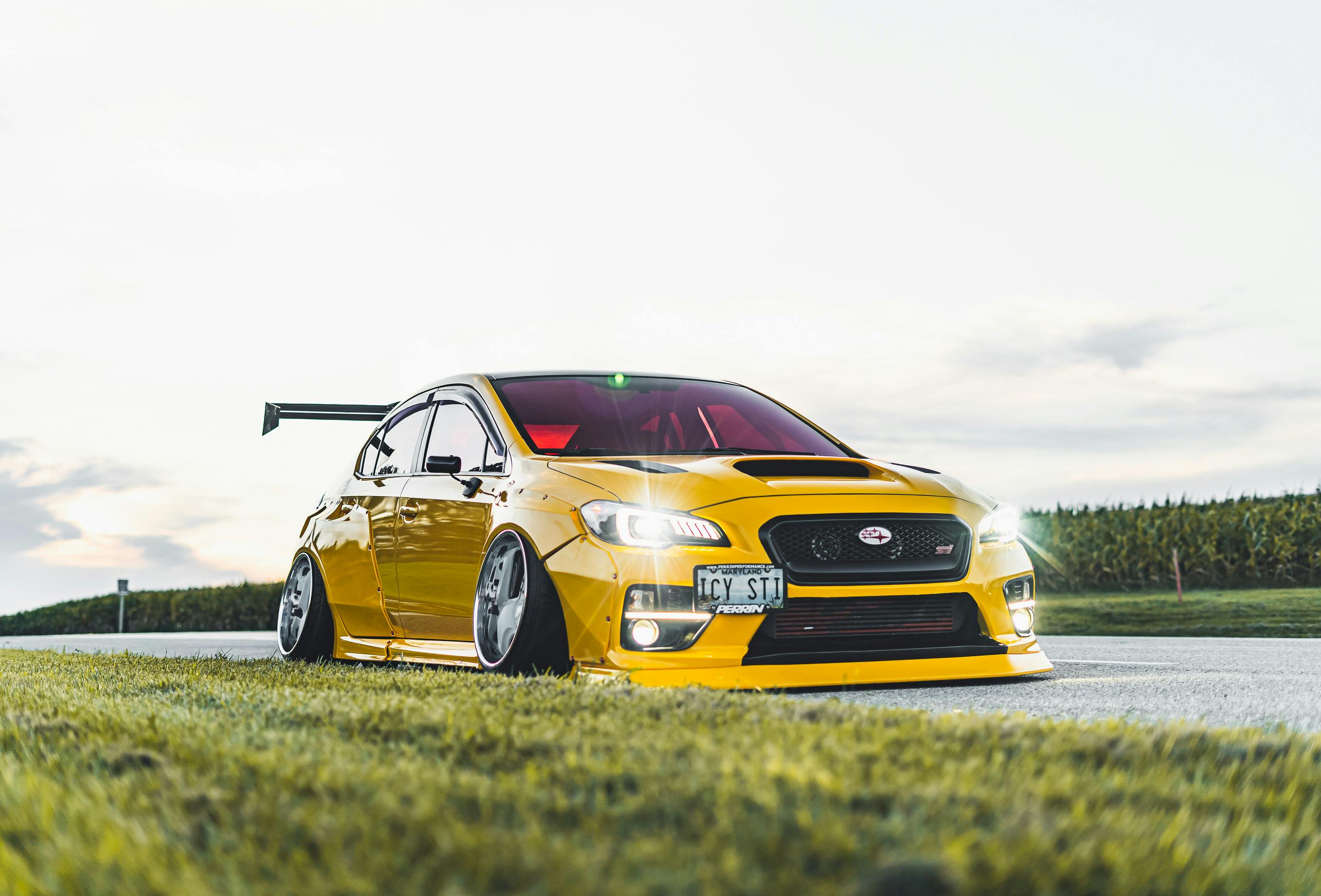 Stunning yellow sports car with a custom kit on a road at sunset, showcasing speed and style.