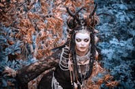 一位迷人的女子身着精致的部落服饰，脸上涂着彩绘，置身于神秘的森林背景之中