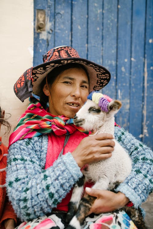 Peruvian female caressing baby lama in yard of aged house
