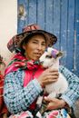 Peruvian female caressing baby lama in yard of aged house
