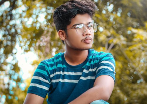 Free Portrait of a young man wearing eyeglasses and a striped shirt, enjoying a sunny day outdoors. Stock Photo