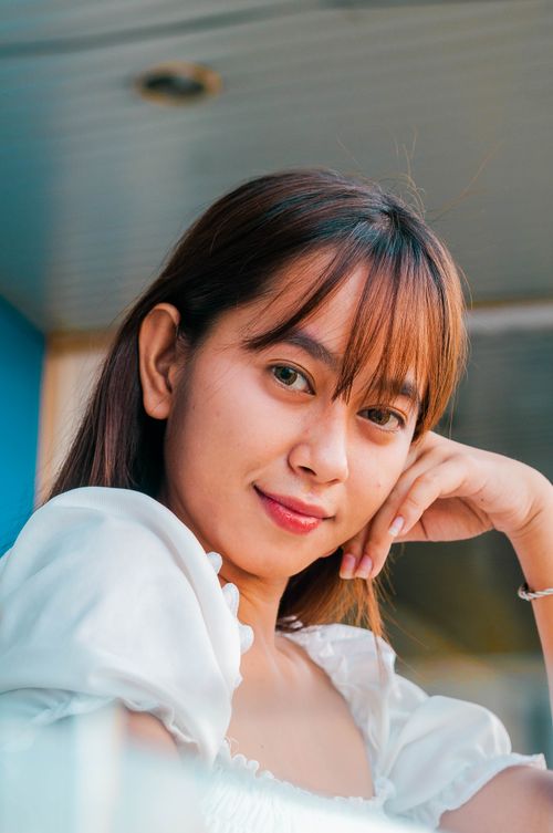 Free Attractive young Asian female in white outfit looking at camera and leaning on hand while standing on balcony near residential house Stock Photo