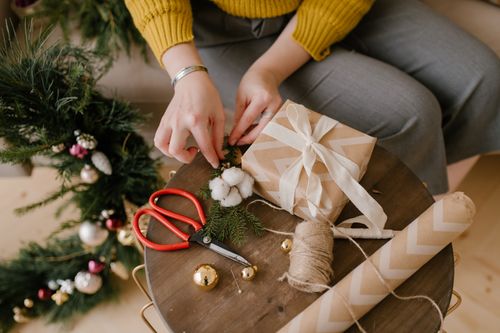 Free Close-up of hands wrapping a Christmas gift with brown paper, surrounded by festive decorations. Stock Photo