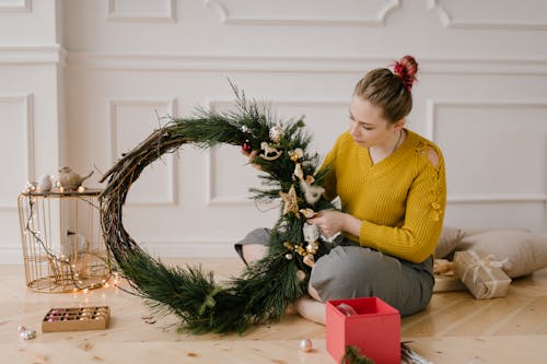 A Woman in Yellow Long Sleeves Holding a Christmas Wreath