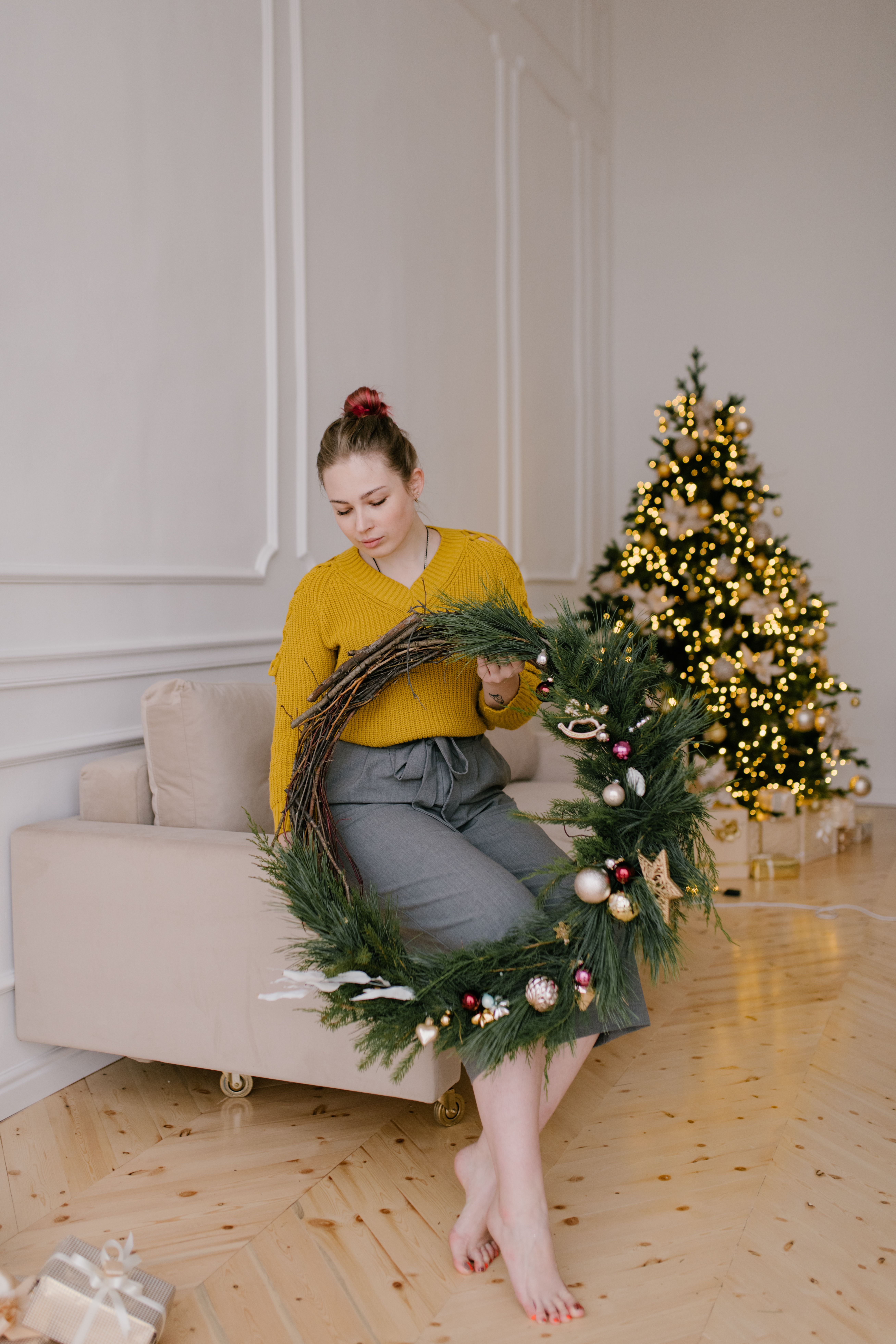 一个女人在舒适的房间里，拿着一只圣诞花圈站在装饰好的树旁