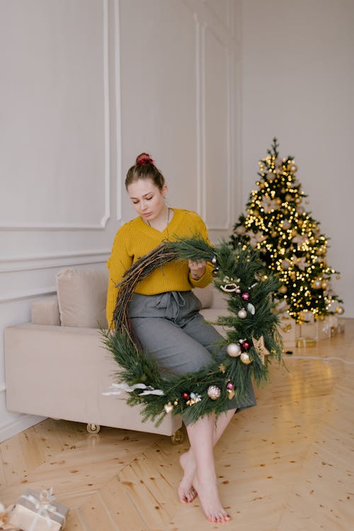 Femme En Pull Jaune Assis Sur Un Canapé Blanc à Côté De L'arbre De Noël Vert