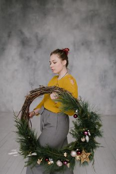 一名妇女穿着芥末色毛衣，在室内拿着圣诞花环准备装饰