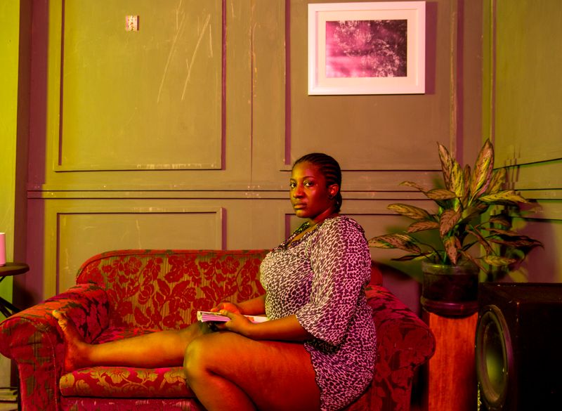 A Black woman sits alone on a couch at home, looking pensive and withdrawn, a scene that reflects the cyclical low mood of premenstrual dysphoric disorder.