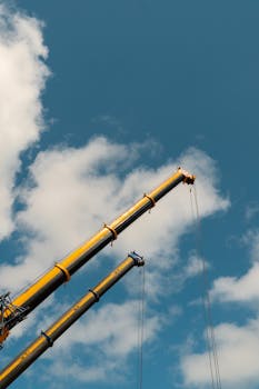 Two towering construction cranes extend against a clear blue sky, showcasing industrial power.