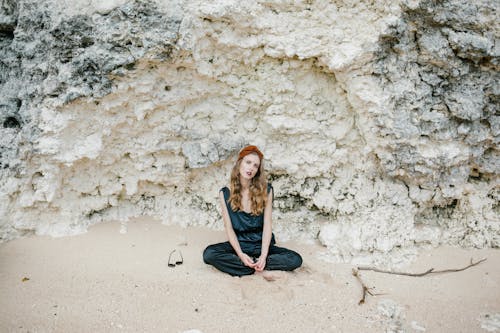 Tranquil woman with bindi in suit sitting in lotus pose on sand against white cliff in daytime