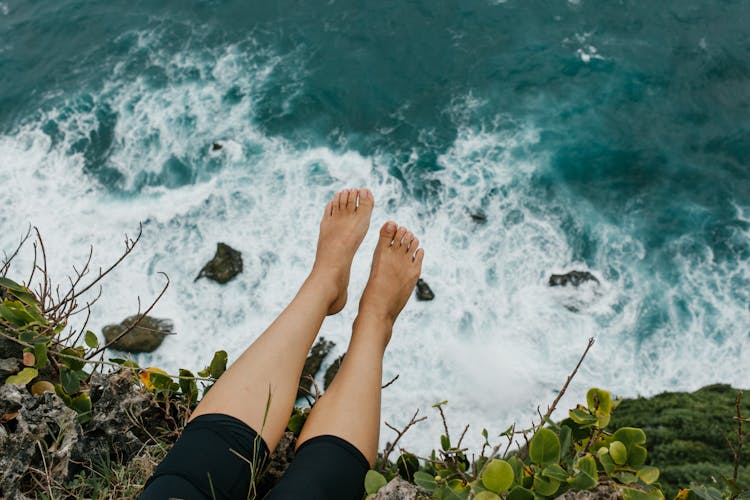 Woman Sitting On Edge Of Cliff Above Foaming Sea