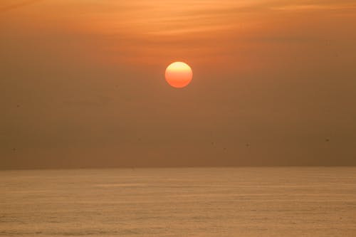 Free Bright orange sun shining over sky under calm endless water of sea at sundown Stock Photo