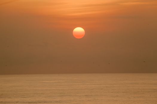 日落时分，明亮的橙色阳光在平静无垠的海面上映照着天空