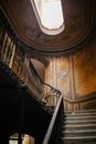 From below of stairway with metal railings in aged building with ornamental walls with sunlight shining through ceiling