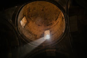 From below of bright sunshine illuminating through window of dome in ancient stone cathedral