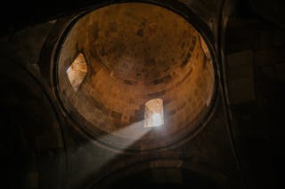 From below of bright sunshine illuminating through window of dome in ancient stone cathedral
