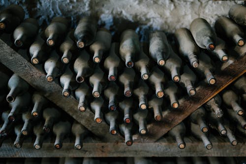 From above of dusty bottles of alcohol drink placed above each other in rows in winery