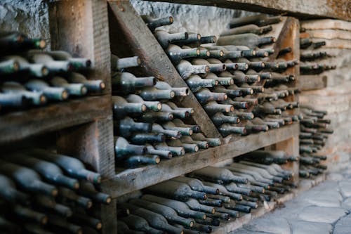 Dusty alcoholic beverage bottles with coiled corks on wooden shelves at wine farm