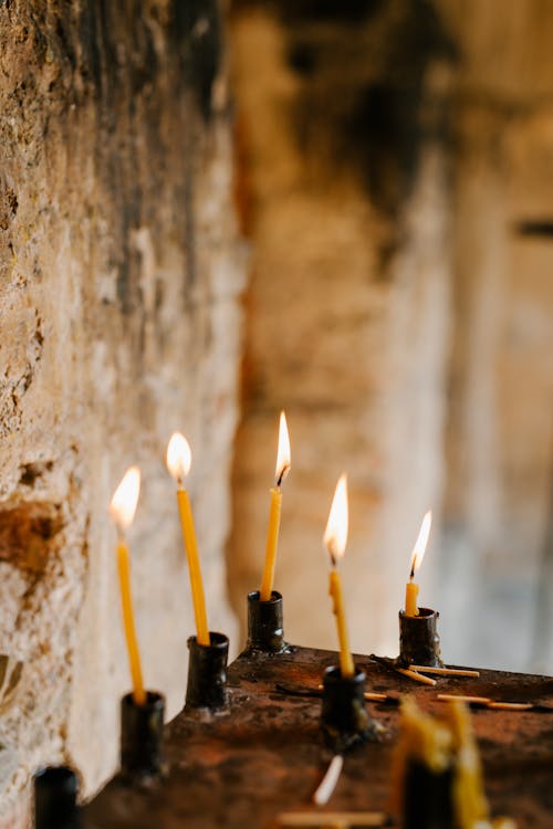 Burning flame of candles placed on shabby surface of ancient sacred place with stone walls