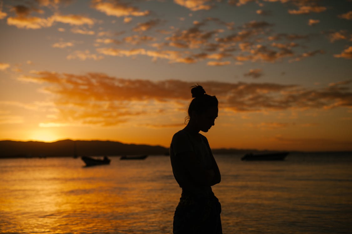 Free Sad woman standing on coast of sea at sunset Stock Photo