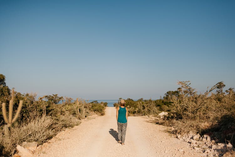 Woman Walking On Dusty Road Towards Sea