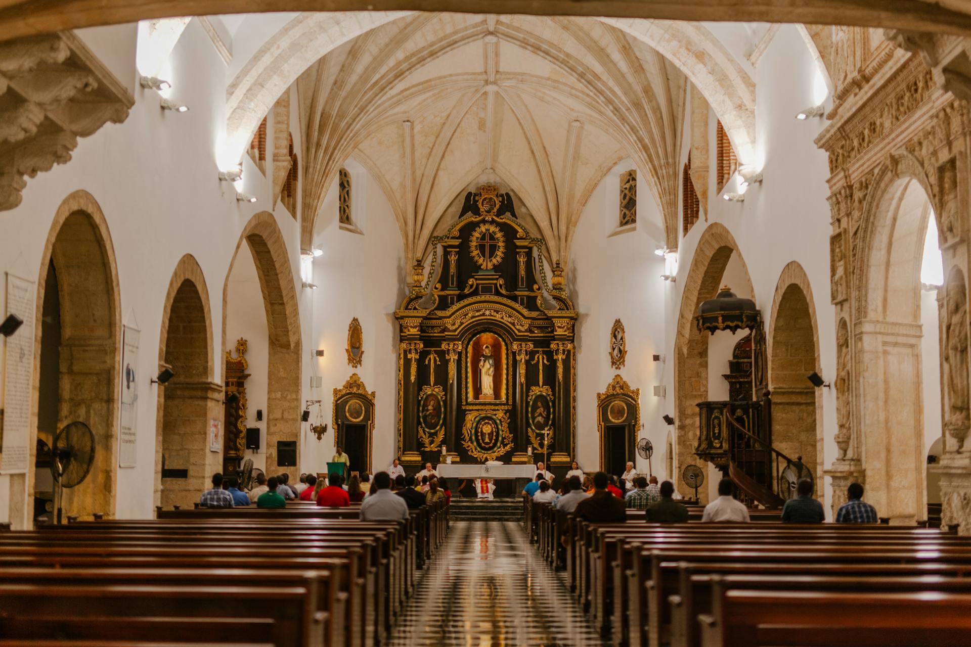 Back view of anonymous religious people sitting on wooden pews near corridor and altar in old stone church