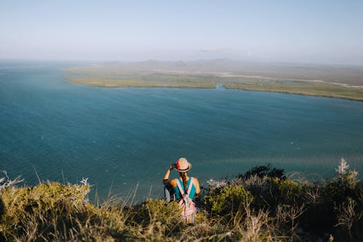 From above back view of anonymous female backpacker enjoying rippled ocean from mount under misty sky