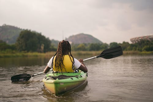 Person in Yellow Life Jacket Sitting on Green Kayak on River
