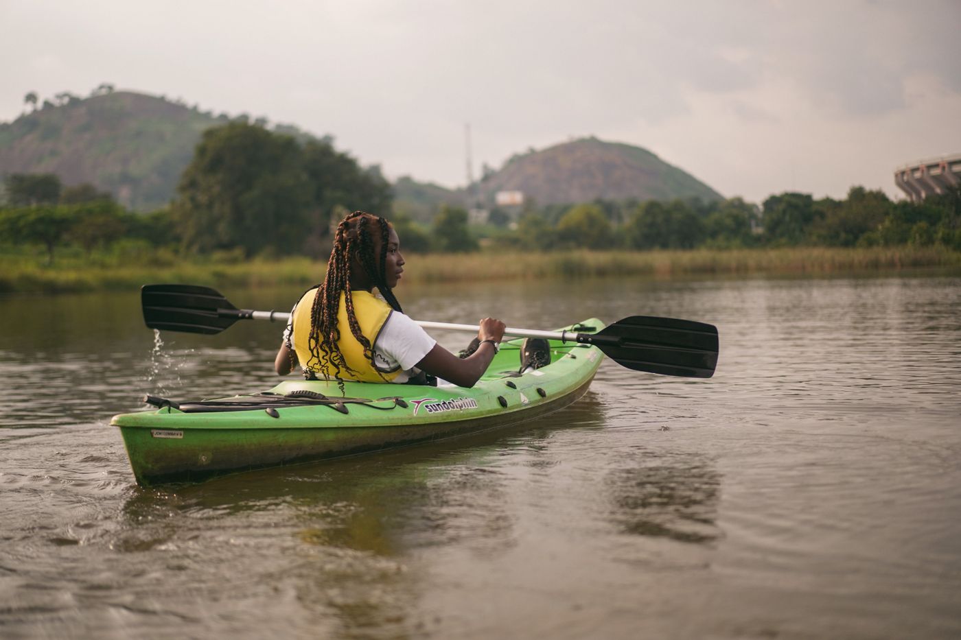 Woman paddling a green kayak across a quiet lake