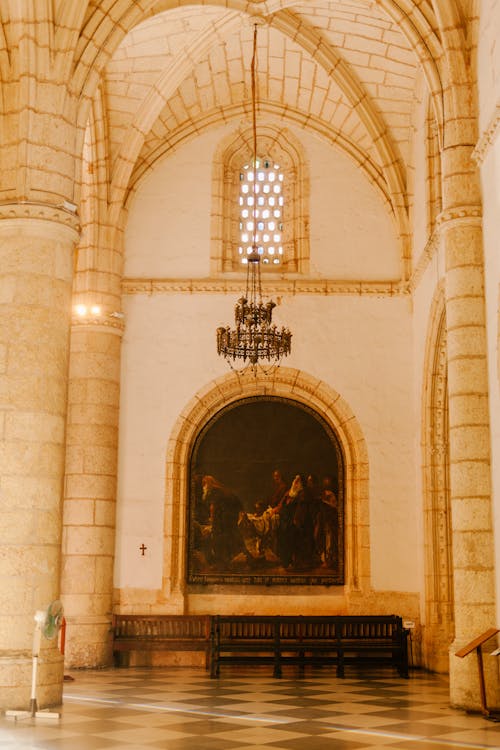 Aged stone cathedral interior with geometric vault above chandelier and floor near mural in sunlight